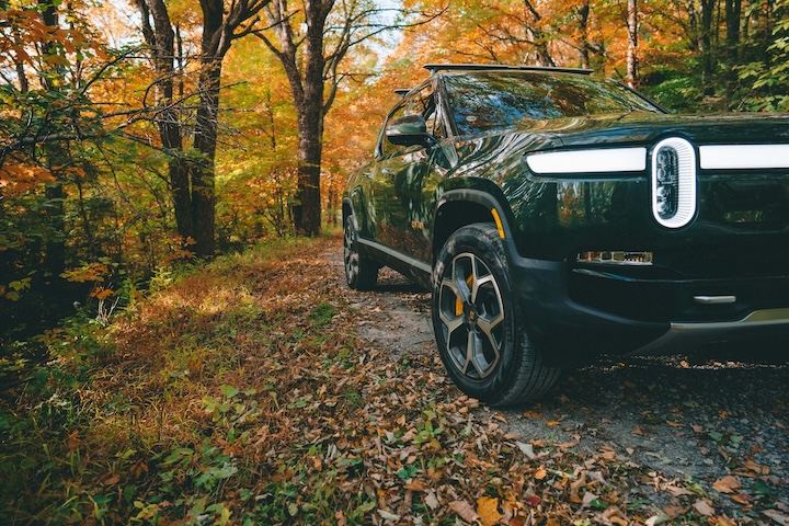 Blue Rivian R1S electric SUV on a forest trail surrounded by autumn foliage